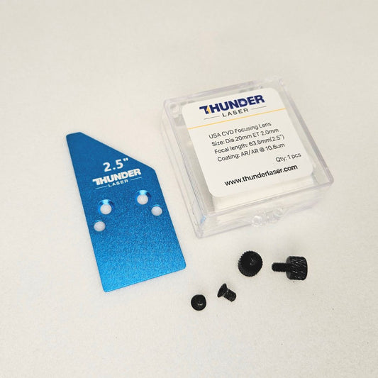 a small square plastic package with a Thunder laser 2.5" inch lens inside for the Thunder Bolt laser cutter. A blue metal plate is beside the plastic package that reads 2.5" and some small black screws