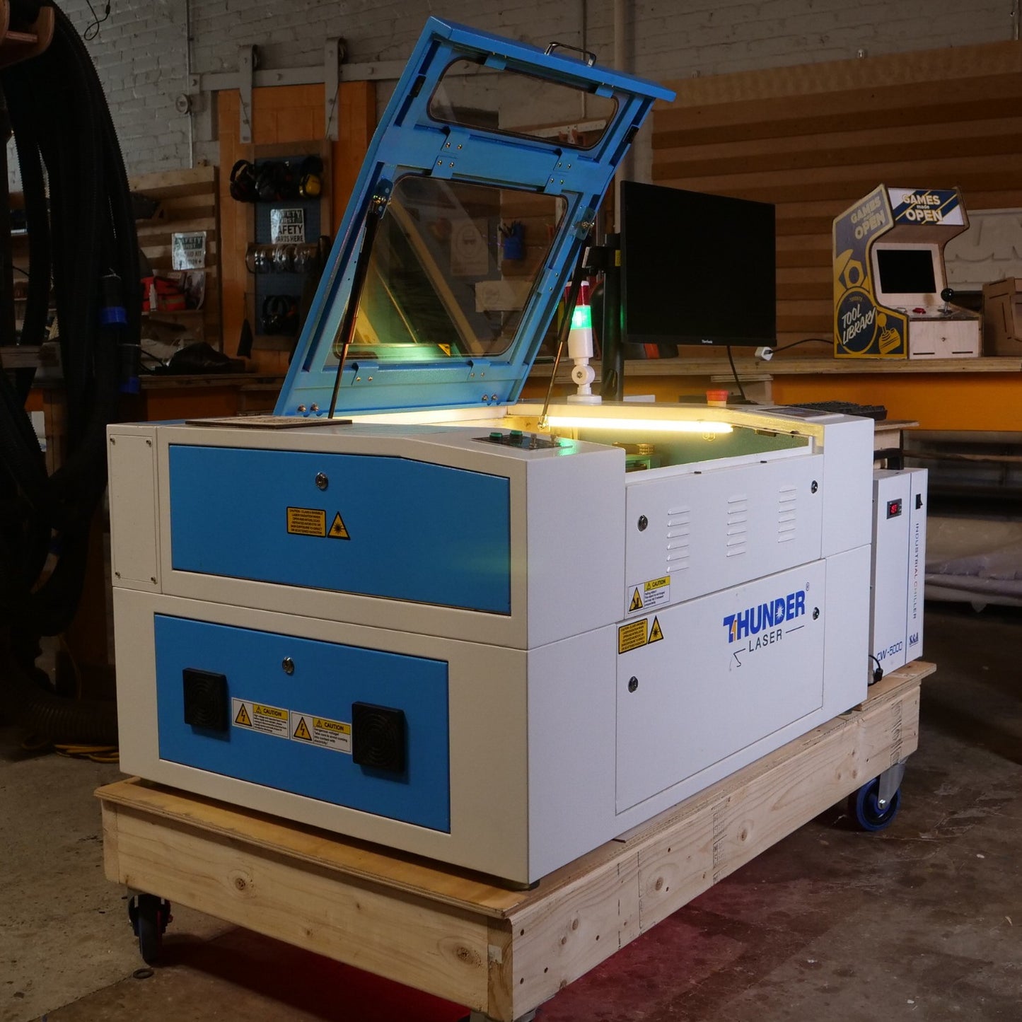 Nova 24 thunder laser machine in a workshop with the lid open. the laser cutter is blue and white metal and the lid has a glass window